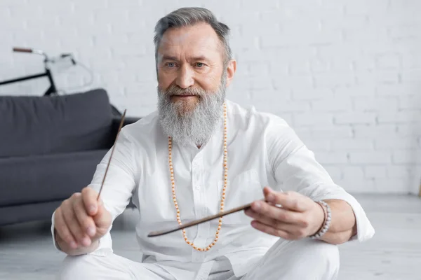 Senior guru man in white shirt and beads holding aroma stick at home — Stock Photo