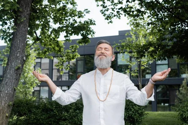 Senior Master Guru mit geschlossenen Augen und offenen Armen meditiert unter Bäumen im Park — Stockfoto