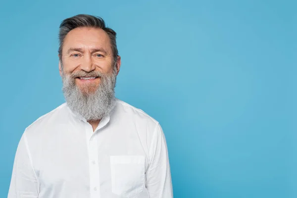 Щасливий бородатий чоловік у білій сорочці дивиться на камеру ізольовано на синьому — стокове фото