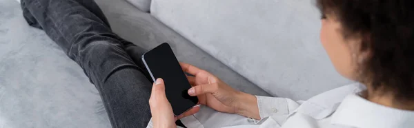 High angle view of curly african american woman holding smartphone with blank screen while sitting on sofa, banner — Stock Photo