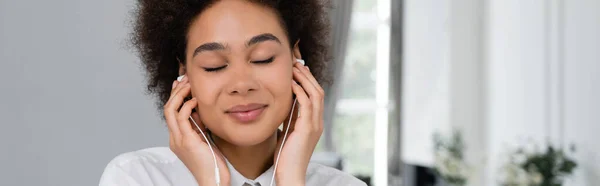 Щаслива афроамериканка з закритими очима слухає музику в дротових навушниках, банер — стокове фото