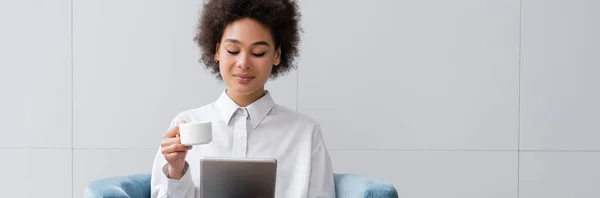 Glückliche afrikanisch-amerikanische Frau hält Tasse Kaffee in der Hand und schaut Film auf digitalem Tablet, Banner — Stockfoto