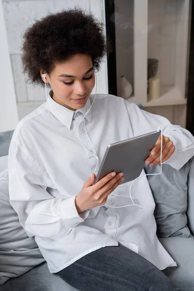 Hochwinkelige Ansicht einer afrikanisch-amerikanischen Frau in kabelgebundenen Kopfhörern, die ein digitales Tablet hält, während sie sich einen Film ansieht — Stockfoto