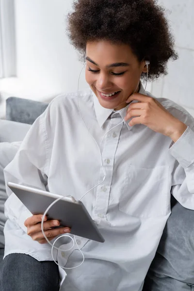 Mujer afroamericana positiva en auriculares con cable sosteniendo la tableta digital mientras ve la película - foto de stock