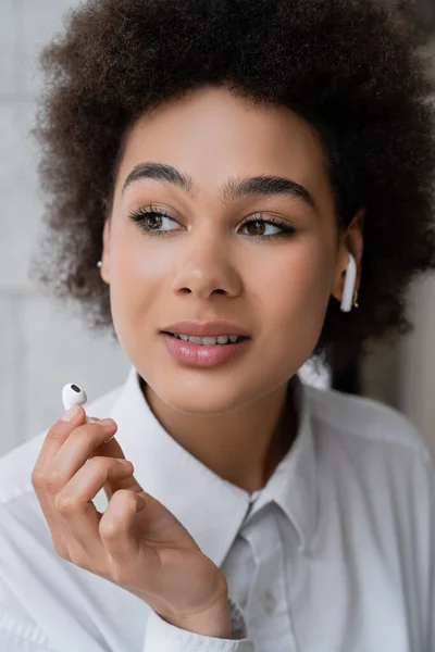 Ritratto di una giovane donna afroamericana che ascolta musica e tiene in mano un auricolare senza fili — Foto stock