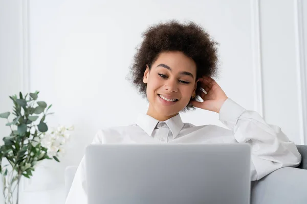 Femme afro-américaine positive utilisant un ordinateur portable tout en travaillant à la maison — Photo de stock