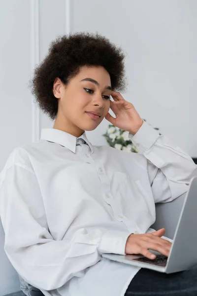 Freelancer afro-americano focado usando laptop enquanto está sentado no sofá em casa — Fotografia de Stock