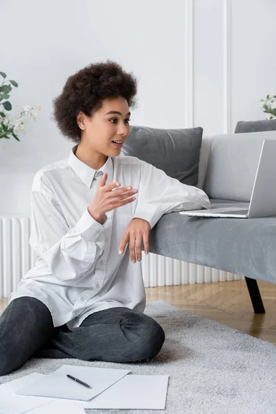 Encaracolado Africano americano mulher gestos durante chamada de vídeo na sala de estar — Fotografia de Stock