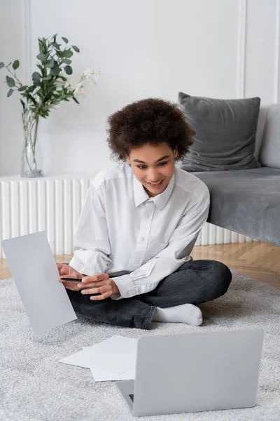 Curly african american woman showing blank document during video call on laptop — Stock Photo