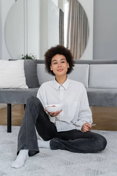 Feliz y joven afroamericana mujer sosteniendo tazón con sabroso desayuno - foto de stock