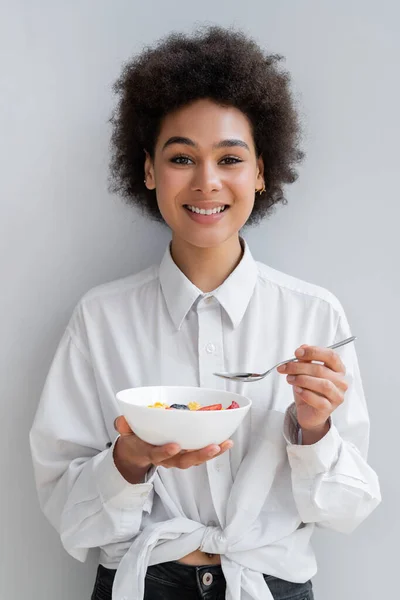 Молодая и веселая африканская американка держит миску с вкусным завтраком на белом — стоковое фото