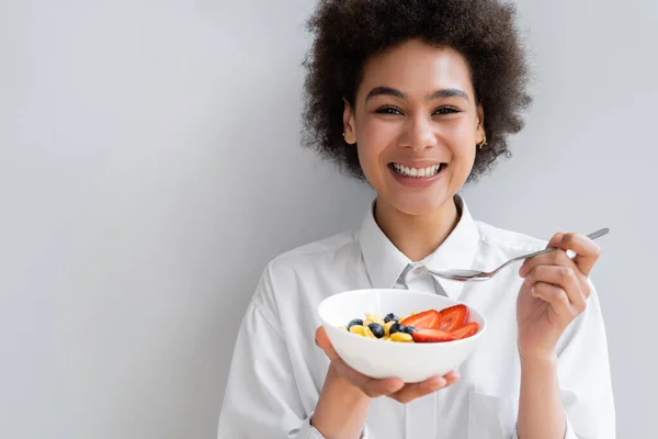 Happy african american woman holding bowl with corn flakes and berries on white — Stock Photo