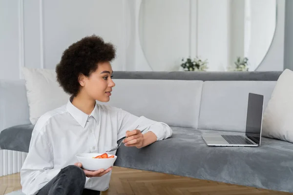 Side view of curly african american woman watching movie while having breakfast in living room — Stock Photo