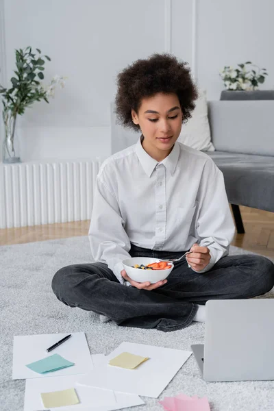 Curly african american freelancer looking at laptop while having breakfast at home — Stock Photo