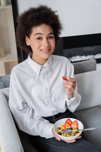 Feliz mulher afro-americana segurando tigela com flocos de milho e morango fresco — Fotografia de Stock