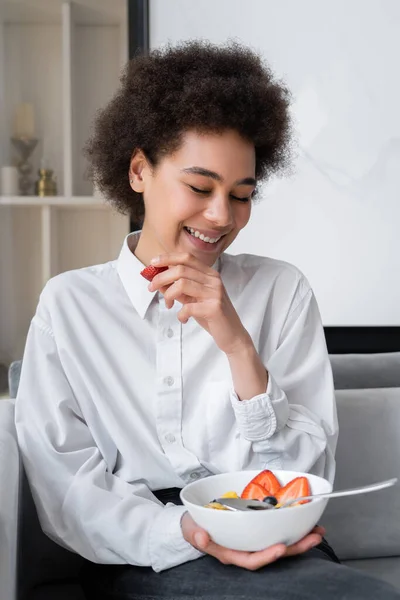Cheerful african american woman holding bowl with corn flakes and fresh strawberry — Stock Photo