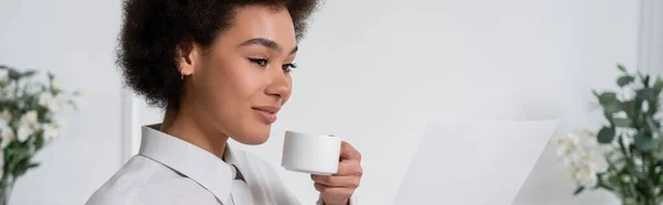 Lockige afrikanisch-amerikanische Frau, die eine Tasse Kaffee hält, während sie leeres Dokument, Banner betrachtet — Stockfoto
