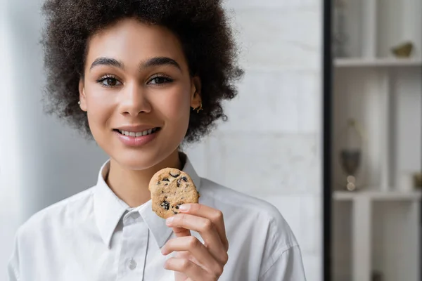 Mujer afroamericana feliz sosteniendo galleta con chispas de chocolate - foto de stock