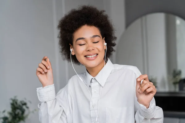 Femme afro-américaine joyeuse avec les yeux fermés écouter de la musique dans des écouteurs filaires — Photo de stock