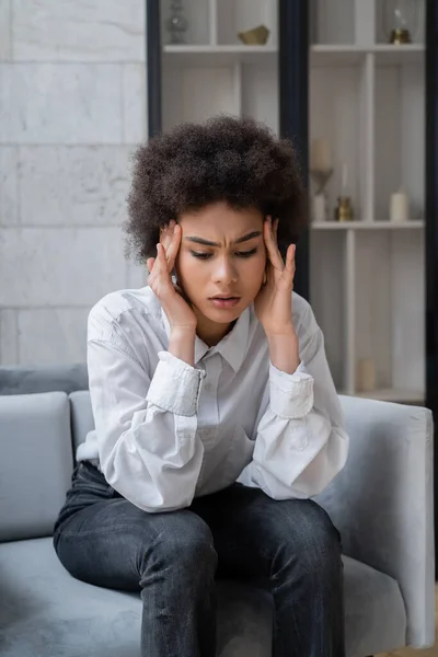 Souligné femme afro-américaine en chemise blanche assis dans le salon — Photo de stock