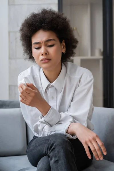 Triste femme afro-américaine en chemise blanche tenant la serviette dans le salon — Photo de stock