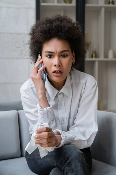 Шокована афроамериканська жінка в білій сорочці говорить на смартфоні — стокове фото