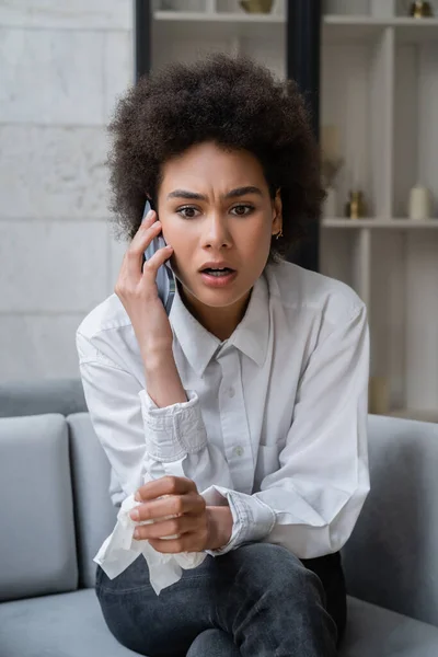 Donna afroamericana scioccata in camicia bianca che parla su smartphone — Foto stock