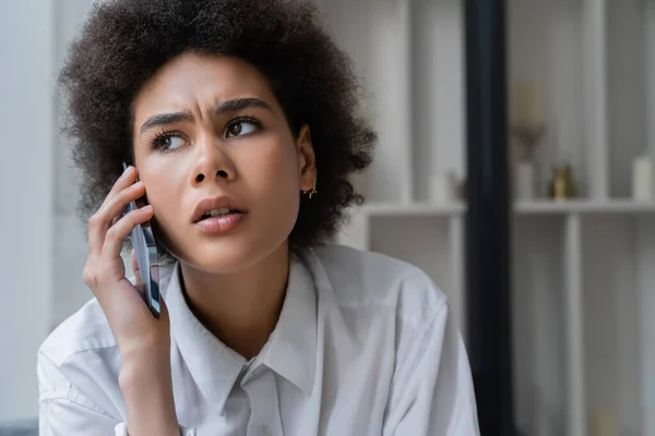 Preocupado mulher americana africana em camisa branca falando no smartphone em casa — Fotografia de Stock