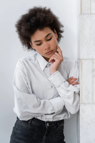 Besorgte Afroamerikanerin in weißem Hemd steht und zu Hause nach unten schaut — Stockfoto