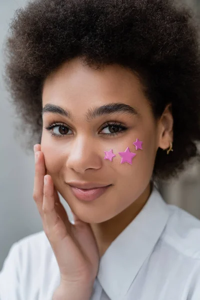 Retrato de mujer afroamericana sonriente con estrellas moradas decorativas en la mejilla - foto de stock