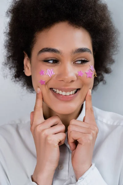 Портрет африканской американки, указывающей пальцами на щеки с декоративными фиолетовыми звездами — стоковое фото