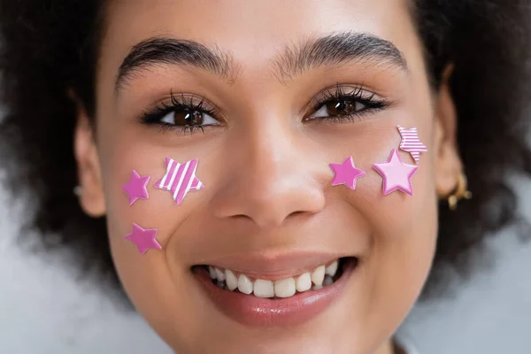 Portrait de femme afro-américaine heureuse avec des étoiles violettes décoratives sur les joues — Photo de stock