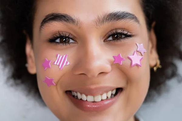 Retrato de mujer afroamericana feliz con estrellas moradas decorativas en las mejillas - foto de stock