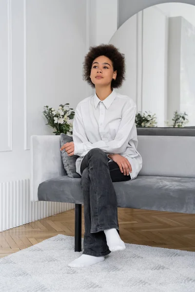 Nachdenkliche Afroamerikanerin sitzt auf grauem Samtsofa im modernen Wohnzimmer — Stockfoto