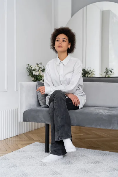 Chère femme afro-américaine assise sur un canapé en velours gris dans un salon moderne — Photo de stock