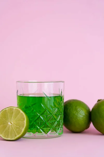 Boisson alcoolisée verte en verre près de limes fraîches sur fond rose — Photo de stock