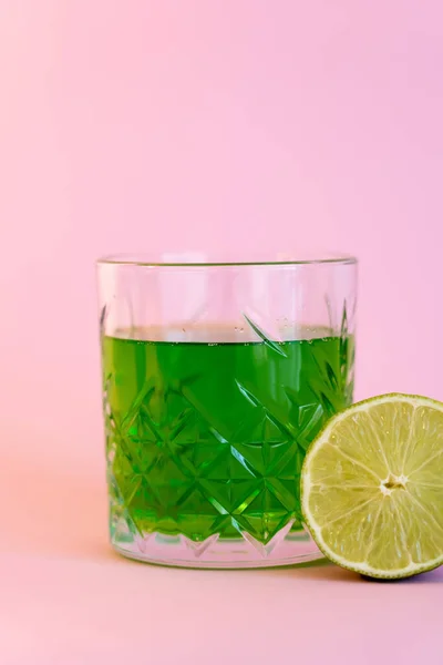 Grünalkoholgetränk im Glas fast zur Hälfte aus frischer Limette auf rosa — Stockfoto