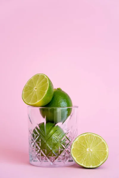 Grüne und frische Limetten in facettiertem Glas auf rosa Hintergrund — Stockfoto