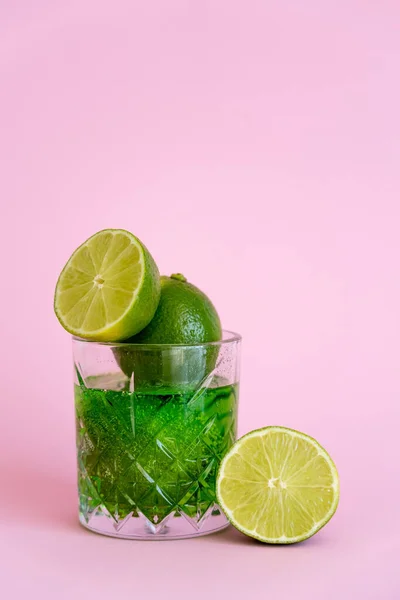 Green and fresh limes in faceted glass with sparkling alcohol drink on pink — Stock Photo