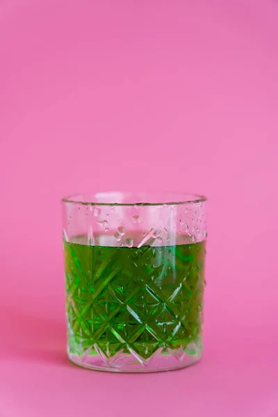 Bebida de álcool verde em vidro facetado com gotas de água em rosa — Fotografia de Stock