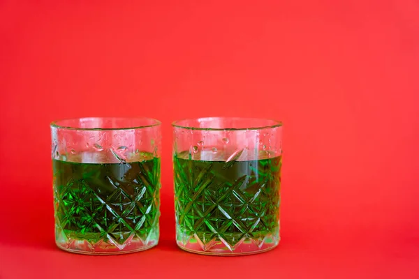 Зелений алкогольний напій у фігурних келихах з краплями води на червоному — стокове фото
