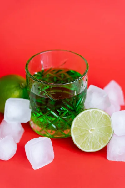 Frozen ice cubes in glass with alcohol green beverage and limes on red — Fotografia de Stock