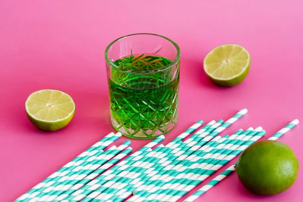 Glass of green alcohol drink near striped paper straws on pink — Stock Photo