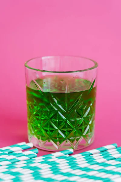 Pailles de papier rayé près du verre à facettes avec cocktail vert sur rose — Photo de stock