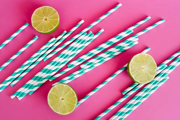 Top view of striped blue and white straws near limes on pink background — Stock Photo