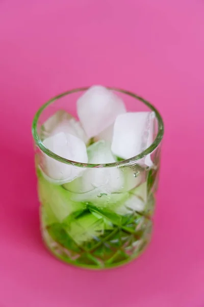 Nahaufnahme gefrorener Eiswürfel im Glas mit grünem Mojito-Drink auf rosa — Stockfoto