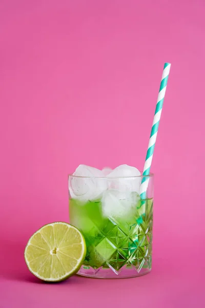 Glaçons congelés en verre avec mojito vert boire près de tranches de citron vert sur rose — Photo de stock