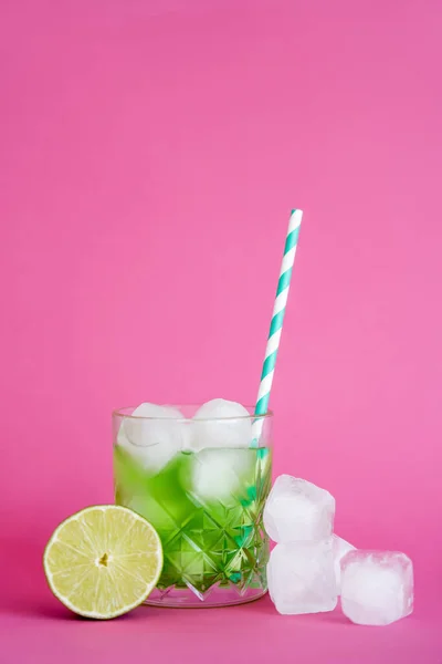 Cubitos de hielo congelados en vidrio con bebida de mojito verde con paja cerca de lima sobre rosa - foto de stock