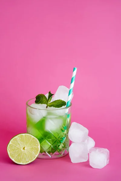 Glaçons congelés en verre avec mojito vert avec paille et menthe près de citron vert sur rose — Photo de stock