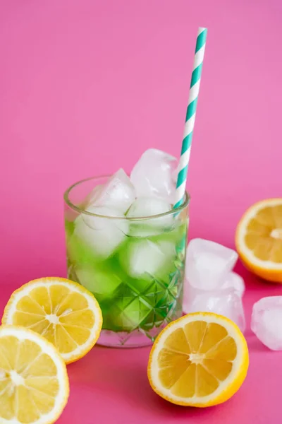 Cubitos de hielo congelados en vidrio con bebida de mojito verde y paja cerca de limones en rosa - foto de stock